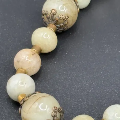 Sale Photo Thumbnail #360: Vintage light green jade or hardstone bead necklace featuring ornate brass or metal end caps and spacer beads.