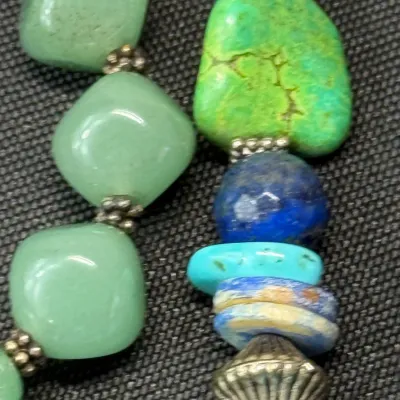 Sale Photo Thumbnail #334: Close-up of a handcrafted beaded necklace featuring green aventurine, turquoise, and lapis lazuli beads strung with silver-tone spacers.