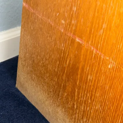Sale Photo Thumbnail #723: Close-up detail of a wooden furniture piece, showing surface scratches, wear to the finish, and a red scuff mark along the grain.