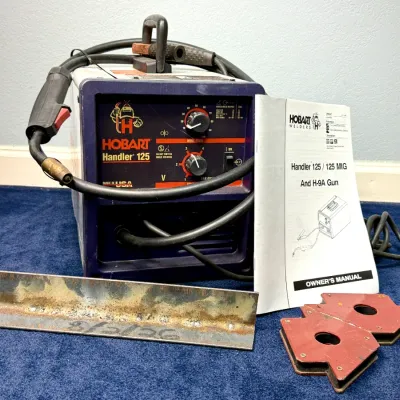 Sale Photo Thumbnail #496: Hobart Handler 125 wire feed welder with attached gun, power cable, ground clamp, owner's manual, arrow welding magnets, and a piece of test steel.