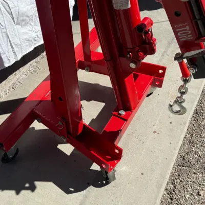 Sale Photo Thumbnail #508: Red 1 1/2-ton hydraulic engine hoist on casters, featuring an adjustable boom with attached chain and hook.