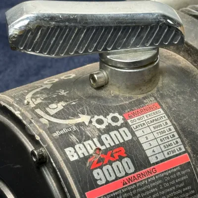 Sale Photo Thumbnail #666: Badland ZXR 9000-lb electric winch showing the clutch handle and warning label, exhibiting minor surface wear and scuffs.