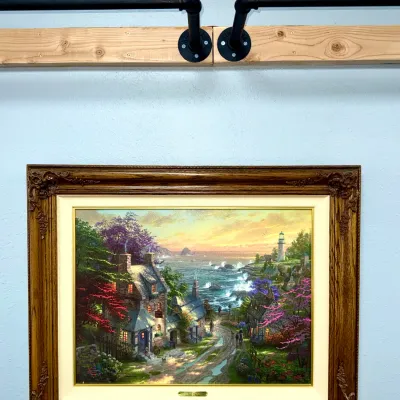 Sale Photo Thumbnail #823: Thomas Kinkade framed art print depicting a seaside cottage landscape, set in a heavy ornate wood frame with a brass title plaque.