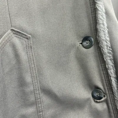 Sale Photo Thumbnail #870: Detail of a vintage grey canvas coat featuring a faux-fur lining trim, front buttons, and double-stitched pocket detailing.