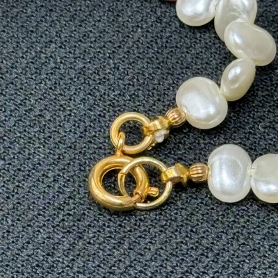 Sale Photo Thumbnail #194: Close-up of a pearl necklace featuring white and pink cultured pearls with a gold spring ring clasp.