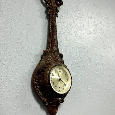 Sale Photo Thumbnail #391: Vintage ornate carved wood-look banjolele-style wall clock with a gold-tone face.