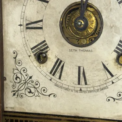 Sale Photo Thumbnail #368: Antique Seth Thomas clock dial featuring Roman numerals, corner spandrel scrollwork, and an exposed escapement window showing the brass movement.