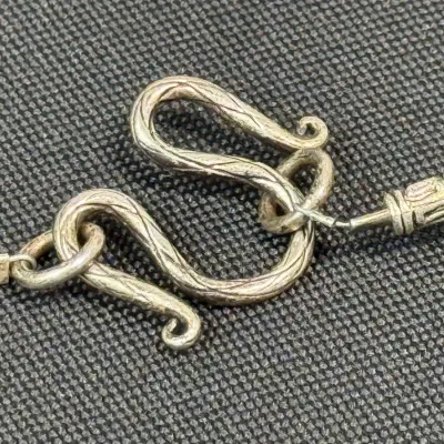 Sale Photo Thumbnail #336: Close-up view of an ornate, textured silver S-hook clasp on a piece of jewelry.