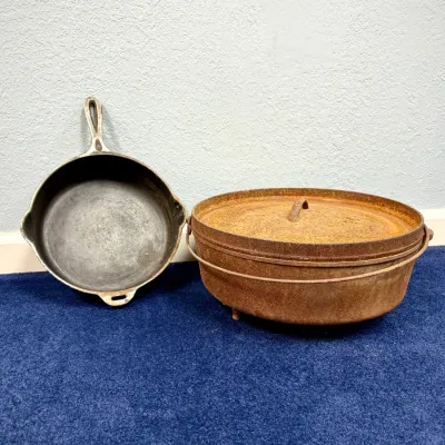 Sale Photo Thumbnail #582: Vintage cast iron skillet alongside a rustic cast iron Dutch oven with lid and bail handle, both displaying surface wear and rust.