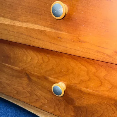 Sale Photo Thumbnail #718: Detail view of a mid-century wooden dresser drawer front with round, dual-tone metal and wood knobs.