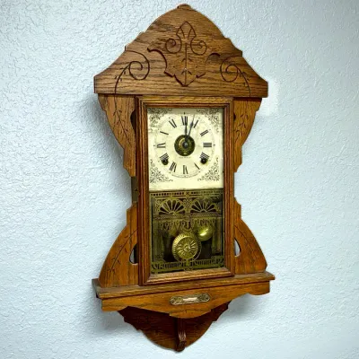 Sale Photo Thumbnail #367: Vintage Seth Thomas oak gingerbread wall clock featuring carved scrollwork details, a brass pendulum, and decorative stencil art on the lower glass pane.