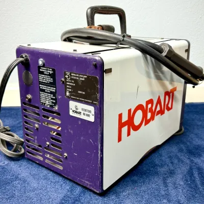 Sale Photo Thumbnail #502: Hobart reconditioned portable welder unit with attached power cord and top handle.
