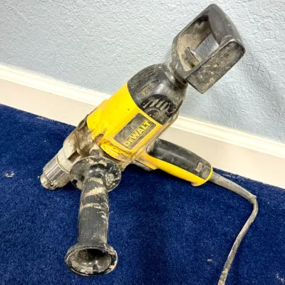 Sale Photo Thumbnail #611: Heavy-duty DeWalt corded electric drill featuring a side handle and top spade handle, showing heavy signs of wear and jobsite dirt.
