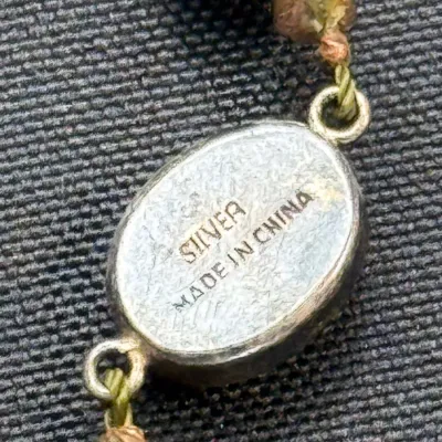 Sale Photo Thumbnail #361: Close-up detail of a silver jewelry clasp stamped with "SILVER MADE IN CHINA," string on green thread alongside beads.