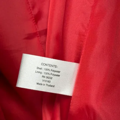 Sale Photo Thumbnail #895: Clothing tag inside a red jacket, indicating a 100% polyester shell and lining, made in Thailand.