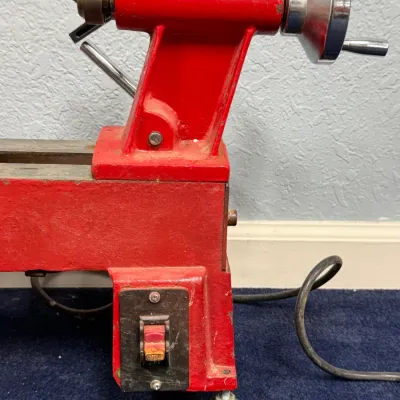 Sale Photo Thumbnail #558: Vintage red metal mini lathe showing tailstock assembly, handwheel, and power switch base.