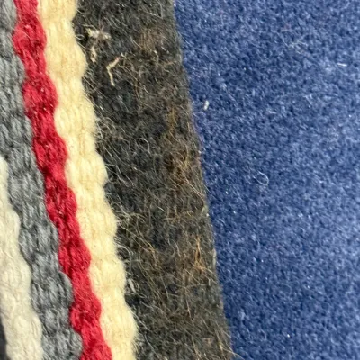 Sale Photo Thumbnail #443: Extreme close-up detail of a hand-woven wool textile featuring striped patterns in red, grey, cream, and dark wool against a solid blue background.