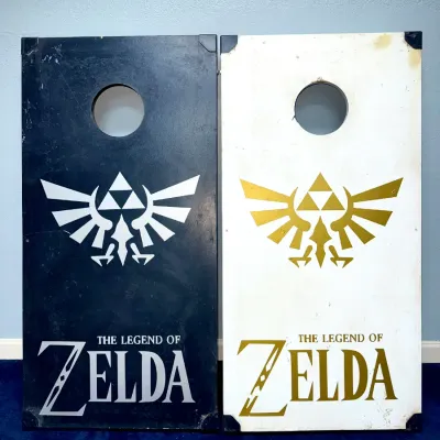 Sale Photo Thumbnail #920: Pair of custom Legend of Zelda-themed wooden cornhole boards featuring silver and gold Royal Crest graphics on black and white backgrounds.