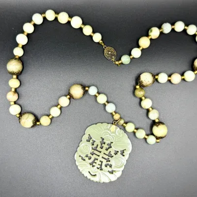 Sale Photo Thumbnail #25: Vintage Asian-style beaded necklace featuring light green and mottled stone beads, ornate brass filigree caps, and a large hand-carved jade pendant with intricate openwork.