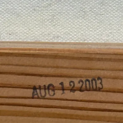 Sale Photo Thumbnail #837: Close-up detail of a date stamp reading 'AUG 1 2 2003' on the wooden edge of an artwork or frame.