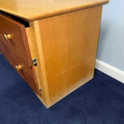 Sale Photo Thumbnail #717: Light-toned wooden filing cabinet or dresser with red-toned drawer fronts and wooden knobs, showing moderate finish wear along the base.