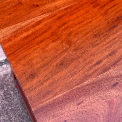Sale Photo Thumbnail #314: Close-up of a warm reddish-brown solid wood tabletop displaying visible surface scratches and natural wood grain.