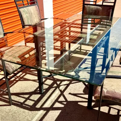 Sale Photo Thumbnail #292: Modern outdoor dining set featuring a rectangular glass-top table with a dark metal frame and six matching armchairs with patterned fabric cushions.
