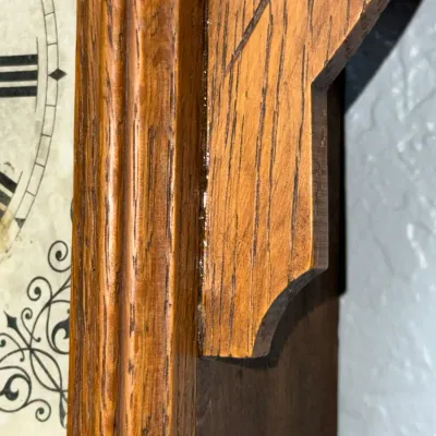 Sale Photo Thumbnail #372: Close-up of a vintage carved oak clock frame displaying a brass hinge pin and detailed wood grain finish.