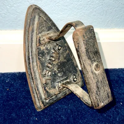 Sale Photo Thumbnail #594: Antique cast iron sad iron featuring embossed lettering, showing heavy patina and age-related wear.