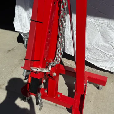 Sale Photo Thumbnail #512: Red hydraulic shop crane or engine hoist in folded position, featuring heavy-duty steel construction, chain attachment, and caster wheels.