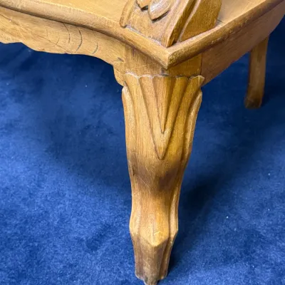 Sale Photo Thumbnail #676: Close-up detail of a vintage wooden chair leg featuring carved leaf motifs and a woven cane seat.
