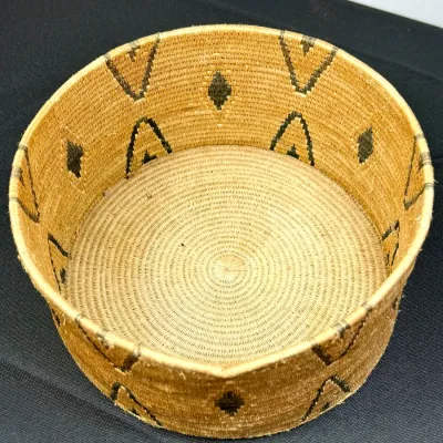 Sale Photo Thumbnail #383: Handwoven cylindrical woven basket featuring dark geometric diamond and arrow motifs around the sides.