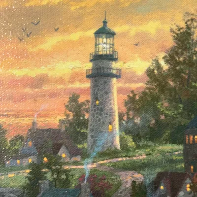 Sale Photo Thumbnail #827: Thomas Kinkade style art print on canvas depicting a glowing stone lighthouse at sunset surrounded by small cottages.