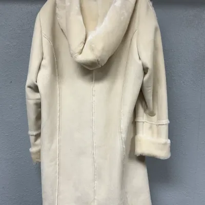 Sale Photo Thumbnail #854: Cream-colored faux shearling or suede hooded coat hanging on a wall hook, featuring fur trim along the hood, cuffs, and hem.
