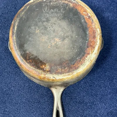 Sale Photo Thumbnail #584: Vintage Wagner Ware Sidney -O- cast aluminum skillet with stylized logo, showing heavy surface wear and discoloration from use.