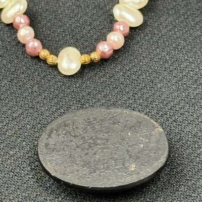 Sale Photo Thumbnail #193: Strand of cultured freshwater pearls in white and pink accents with gold-tone spacer beads, displayed alongside a dark oval cabochon or stone.