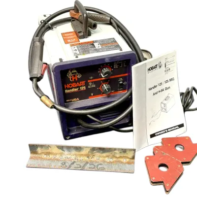 Sale Photo Thumbnail #40: Hobart Handler 125 wire-feed welder with attached MIG gun, ground clamp, original owner's manual, magnetic welding clamps, and a scrap metal test piece.