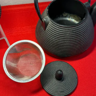 Sale Photo Thumbnail #465: Black cast iron Japanese-style tetsubin teapot with ribbed texture, matching lid, and removable mesh tea infuser basket.