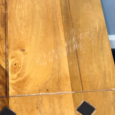 Sale Photo Thumbnail #737: Close-up detail of a wooden tabletop featuring inlaid dark diamond accents, natural wood grain, and visible surface scratches and wear.