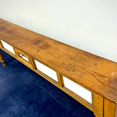 Sale Photo Thumbnail #277: Rustic long wooden console table or workbench featuring a distressed natural finish, turned legs, white side panel inserts, and a center drawer with a metal pull.