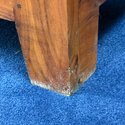 Sale Photo Thumbnail #253: Close-up detail of a solid wood furniture leg with pegged joinery resting on blue carpet, showing minor scuffing and finish wear near the base.
