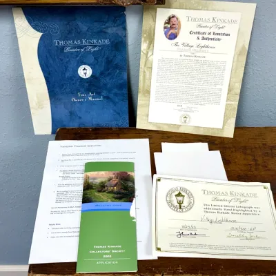 Sale Photo Thumbnail #816: Thomas Kinkade artwork documentation including Certificates of Authenticity, Owner's Manual, and Collector's Society application brochure for 'The Village Lighthouse'.