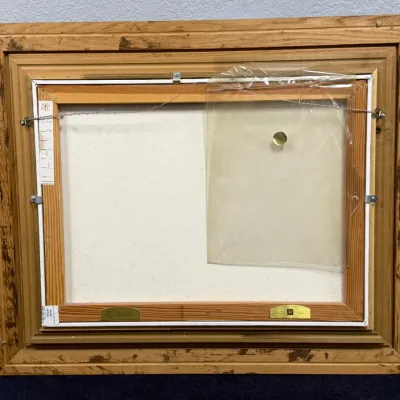 Sale Photo Thumbnail #832: Back view of a framed stretched canvas artwork showing hanging wire, gallery tags, and a protective plastic sleeve on a wooden frame.