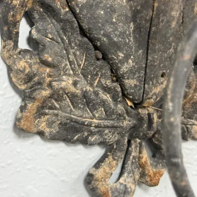 Sale Photo Thumbnail #650: Vintage cast iron wall piece featuring detailed leaf and ribbon motifs with a distressed, rustic patina.