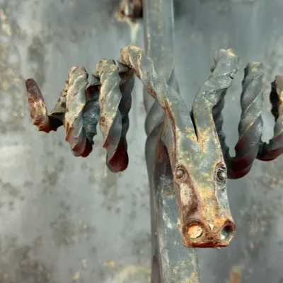 Sale Photo Thumbnail #414: Hand-forged wrought iron wall hook featuring a stylized goat head design with twisted spiraling horns, displaying a weathered patina and light surface rust.