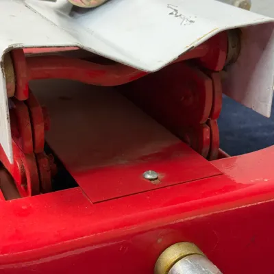Sale Photo Thumbnail #529: Close-up view of a red and white scissor lift table or jack mechanism, showing the internal frame, drive screw socket, and ratchet strap attachment.