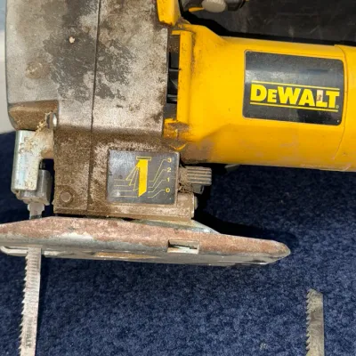 Sale Photo Thumbnail #601: DeWalt corded orbital jigsaw showing heavy cosmetic wear and sawdust accumulation, with an attached blade and extra loose blades.