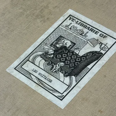 Sale Photo Thumbnail #433: Vintage bookplate inside a cloth-bound book, featuring an illustration with the text 'Ye-Librarie Of Les Whitaker'.