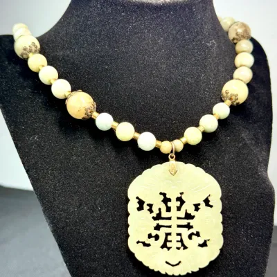 Sale Photo Thumbnail #363: Vintage Asian-style beaded necklace featuring a large, intricately carved pale green jade pendant depicting a longevity symbol and bats, strung with complementary stone and accent beads.
