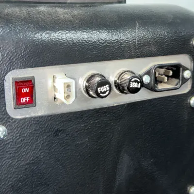Sale Photo Thumbnail #543: Control panel of an electronic device featuring a red power rocker switch, two fuse holders, a multi-pin connector, and a standard IEC power inlet on a textured black housing.